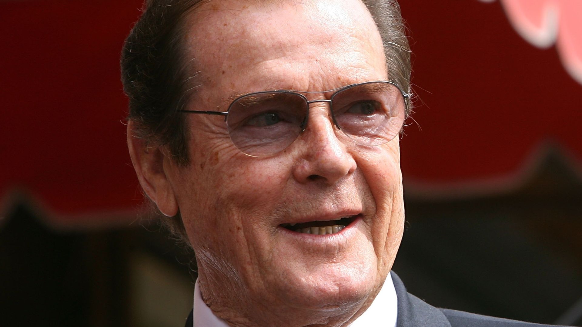Sir Roger Moore smiling looking to the right wearing tinted glasses
