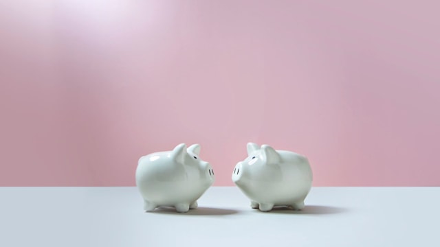 Close up of two white face to face piggy bank on empty pink and grey background.