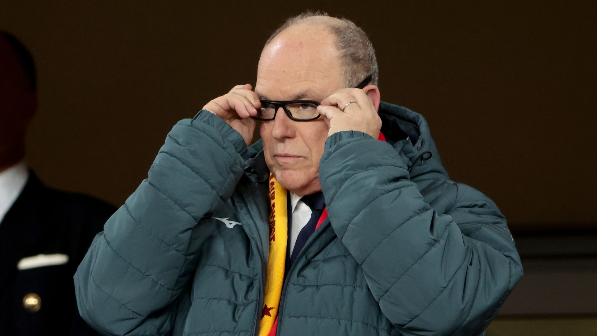 Prince Albert adjusting his glasses while wearing a puffer coat