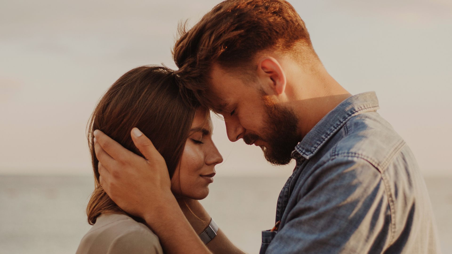 Young couple at the beach pressing foreheads together