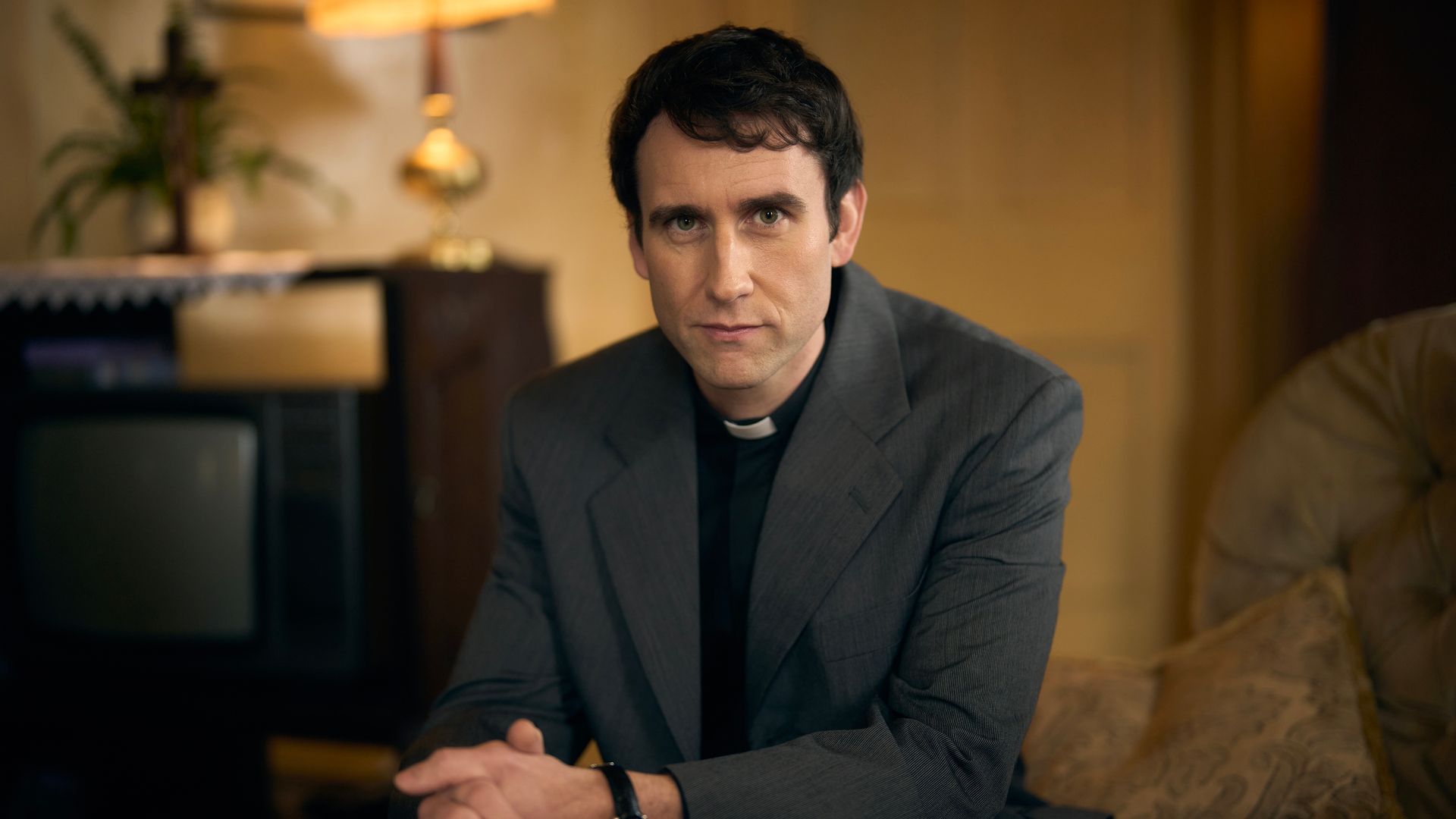 man in vicar's collar sitting in chair