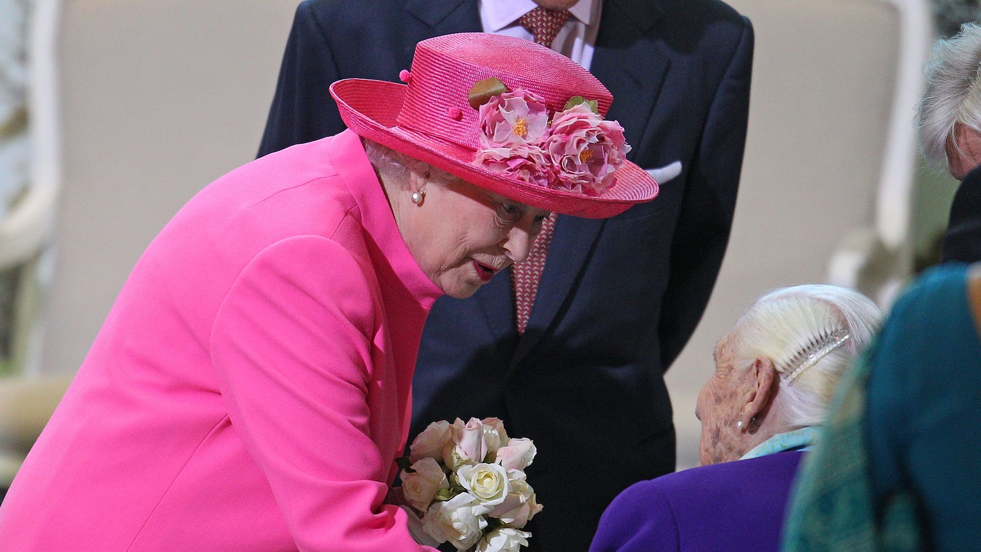 The Queen holding a bunch of flowers and speaking to an elderly woman