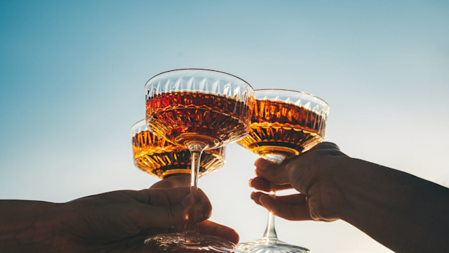 A close-up shot of friends clinking glasses at sunset