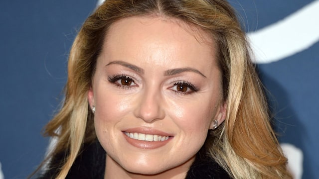 Ola Jordan smiling whilst wearing a black fur coat 