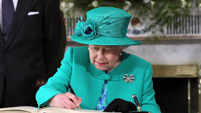 queen in green outfit signing a book