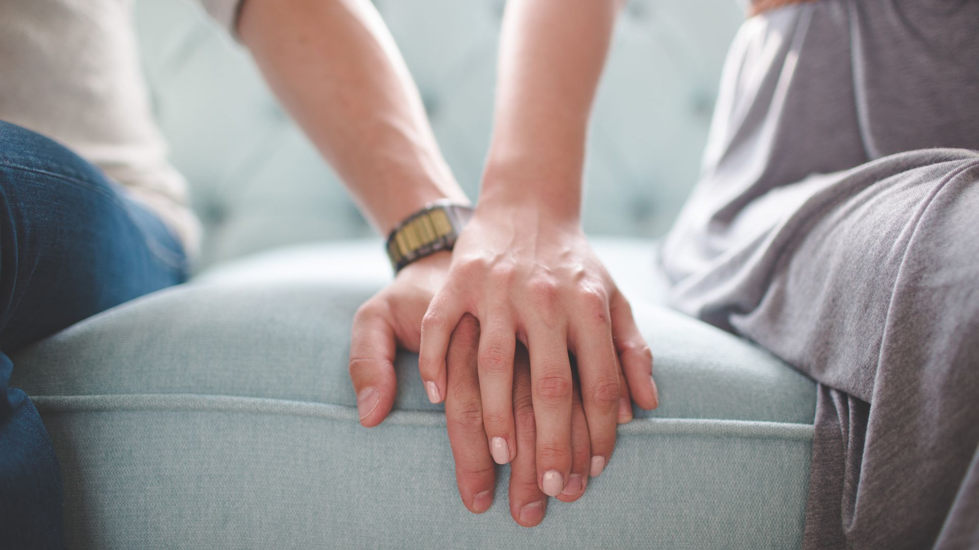 Waist photo of man and woman holding hands while sitting on a couch