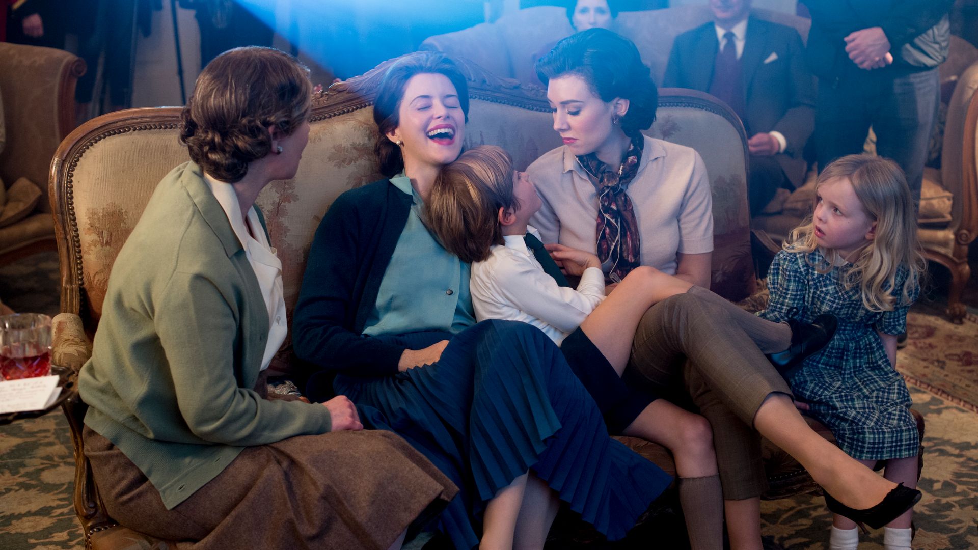 Cast of The Crown season one in character laughing on a sofa