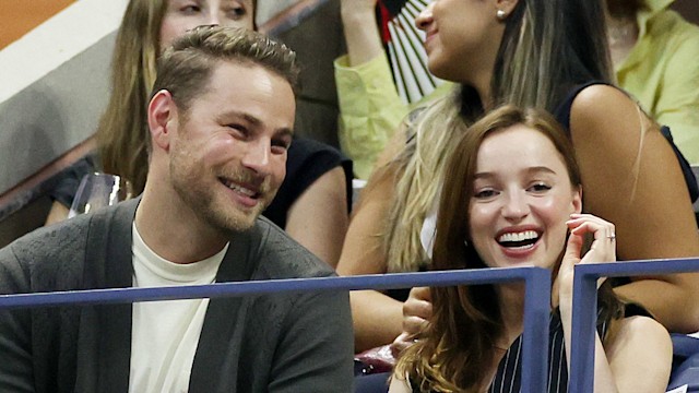 Phoebe Dynevor and Cameron Fuller laughing and sitting down