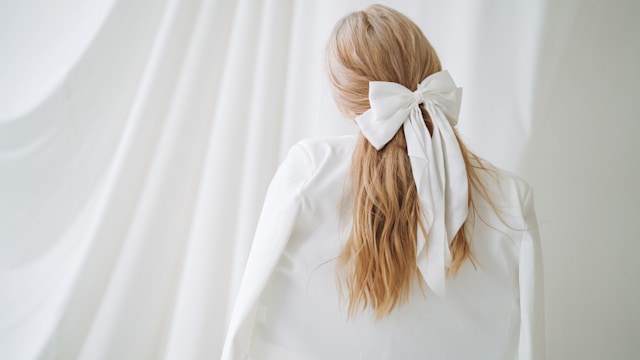 Young woman with long blonde hair and white bow in evening dress on white background