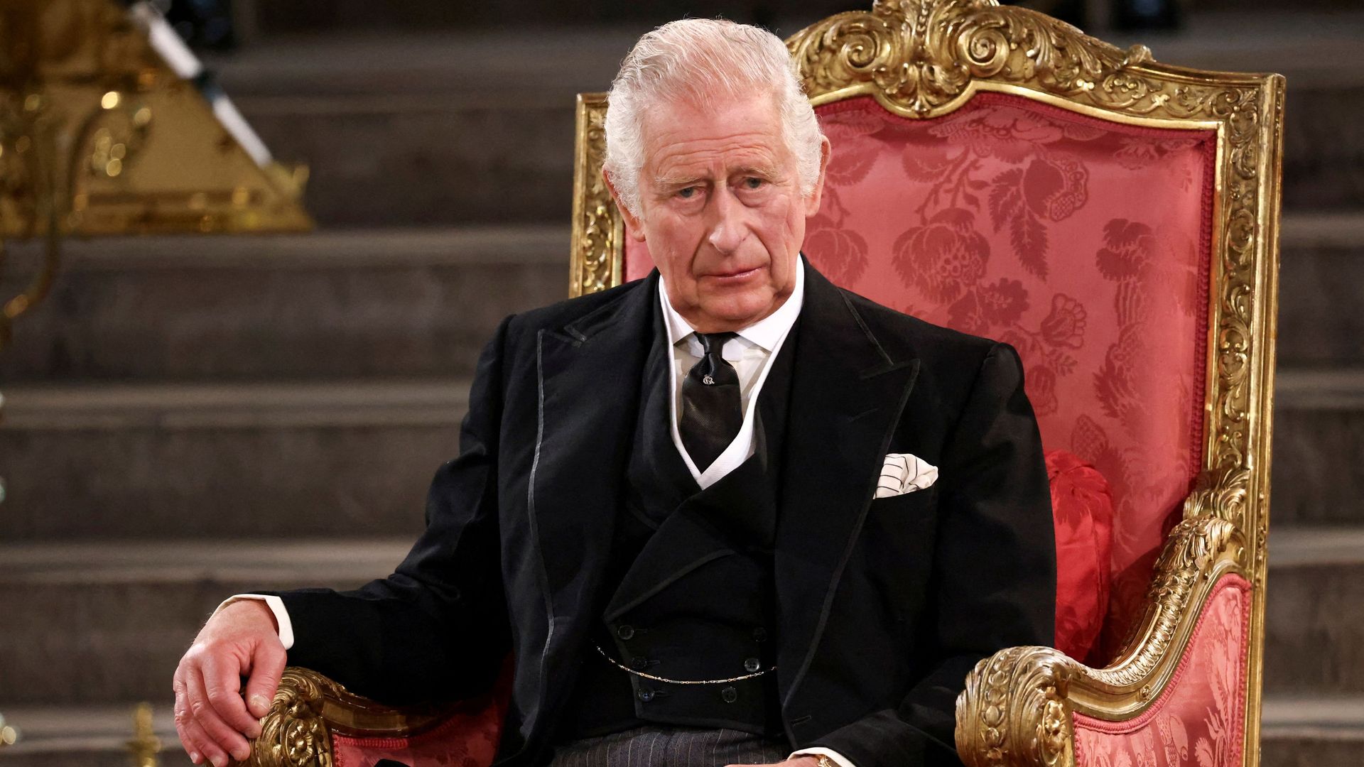 King Charles in a black suit on a red throne