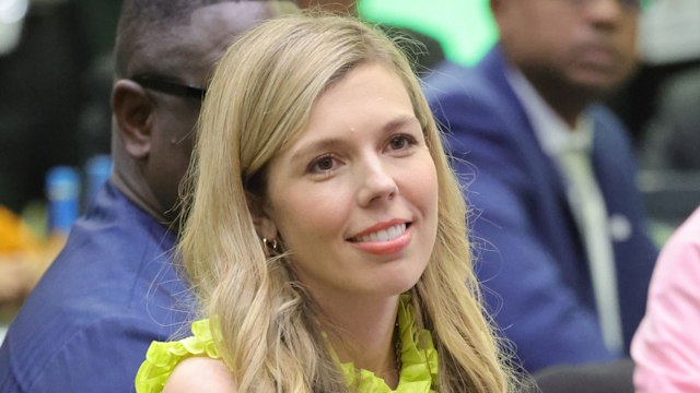 Carrie Johnson sitting in a yellow blouse and blue skirt