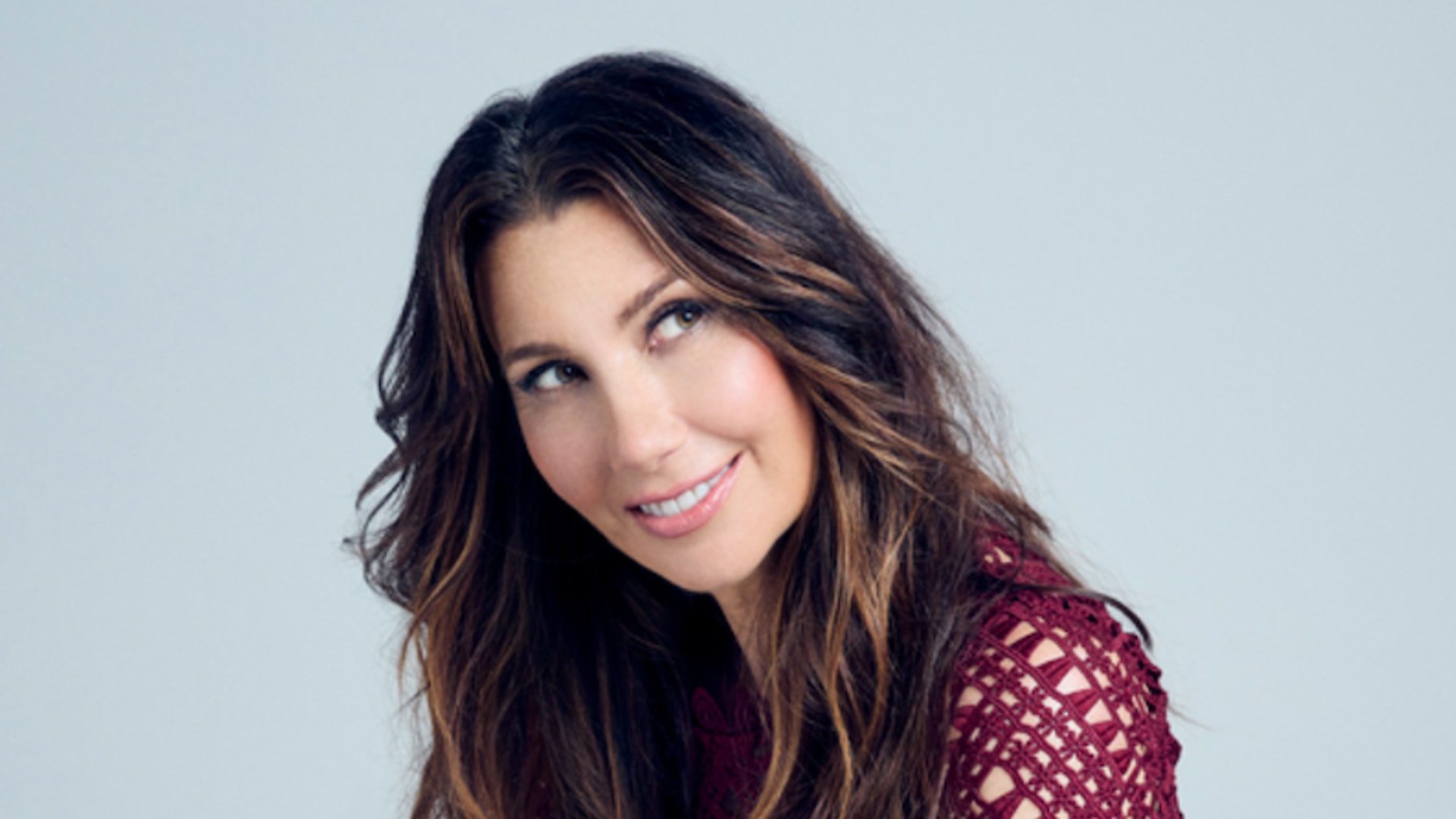brunette woman in a burgundy dress looking to the side and smiling 