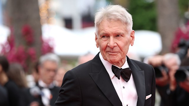 Harrison Ford in a tuxedo looks to his right while on the red carpet