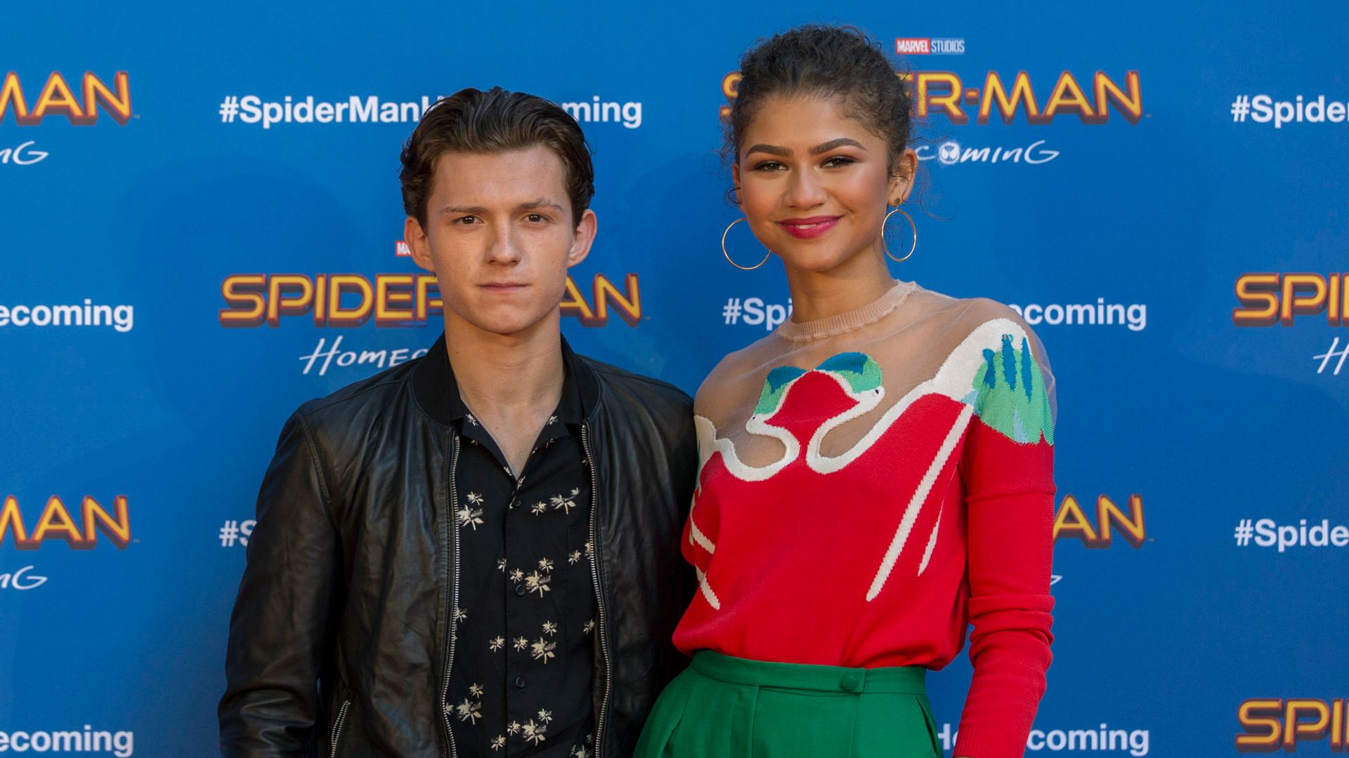 Zendaya and Tom posing in front of a Spider-Man Homecoming billboard
