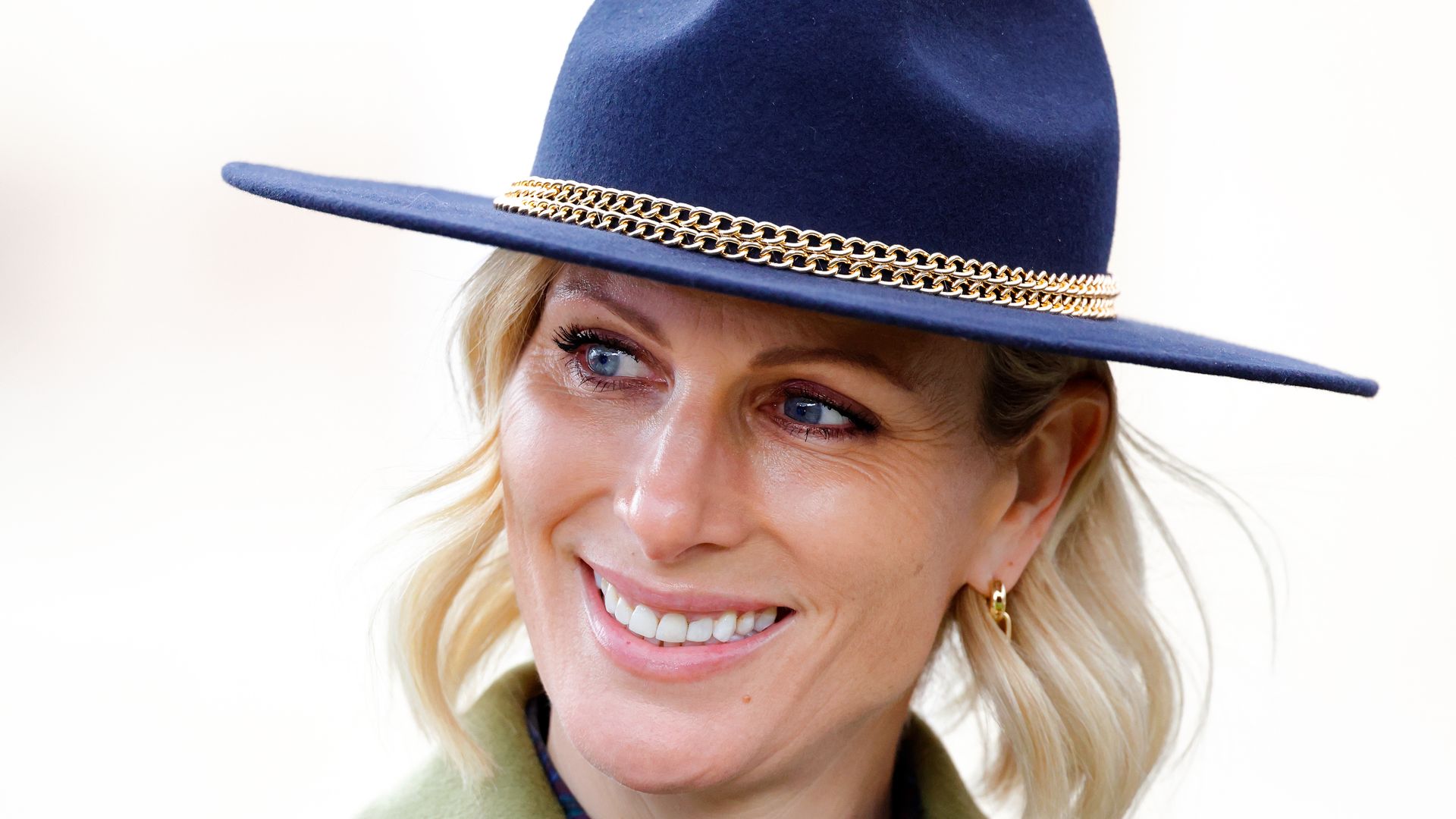 Zara Tindall in khaki coat and navy fedora looking to left