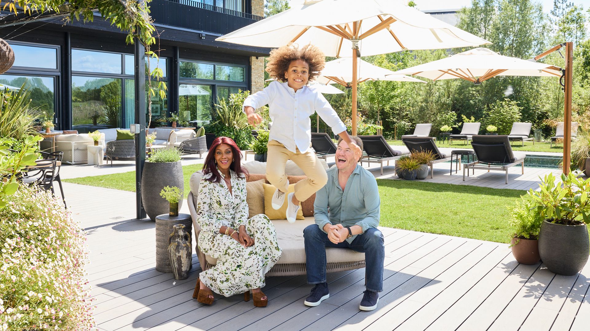 mother and father with their young son jumping off a sofa