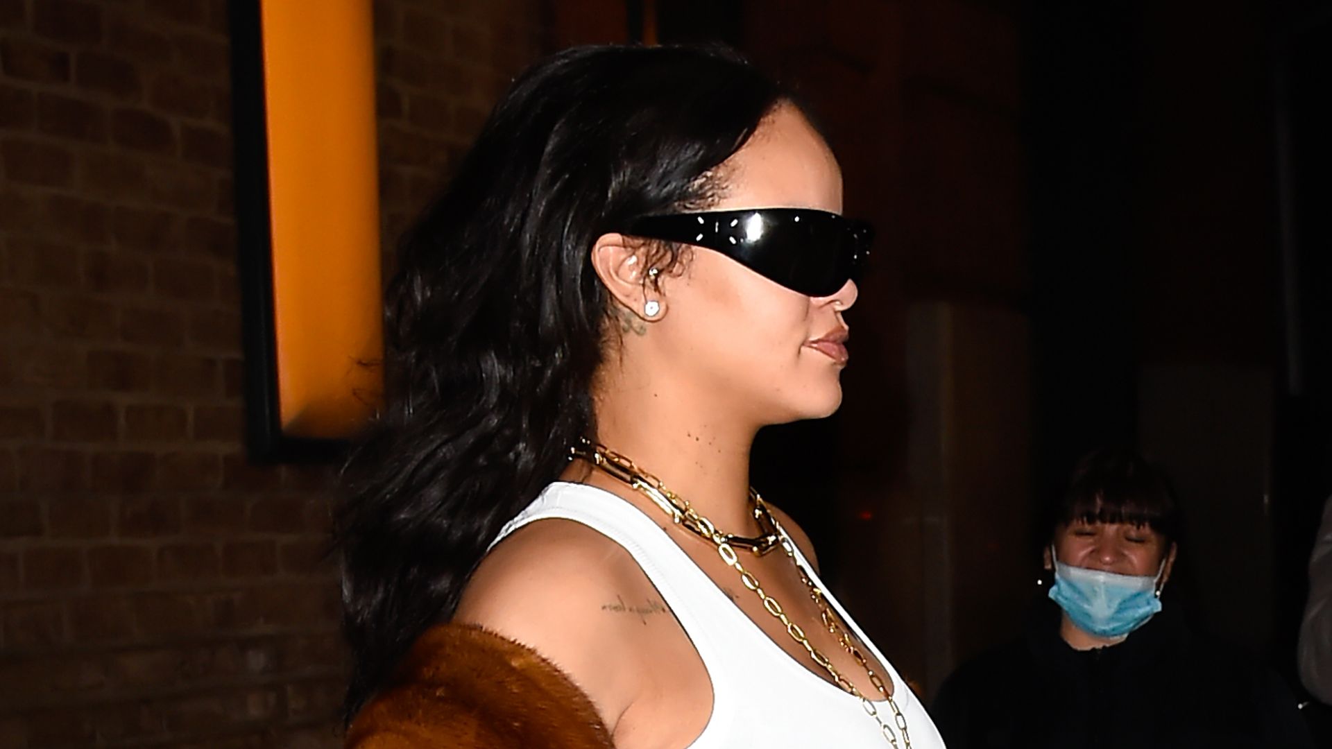 Rihanna wearing a fur coat, sunglasses, a white vest and baggy jeans 