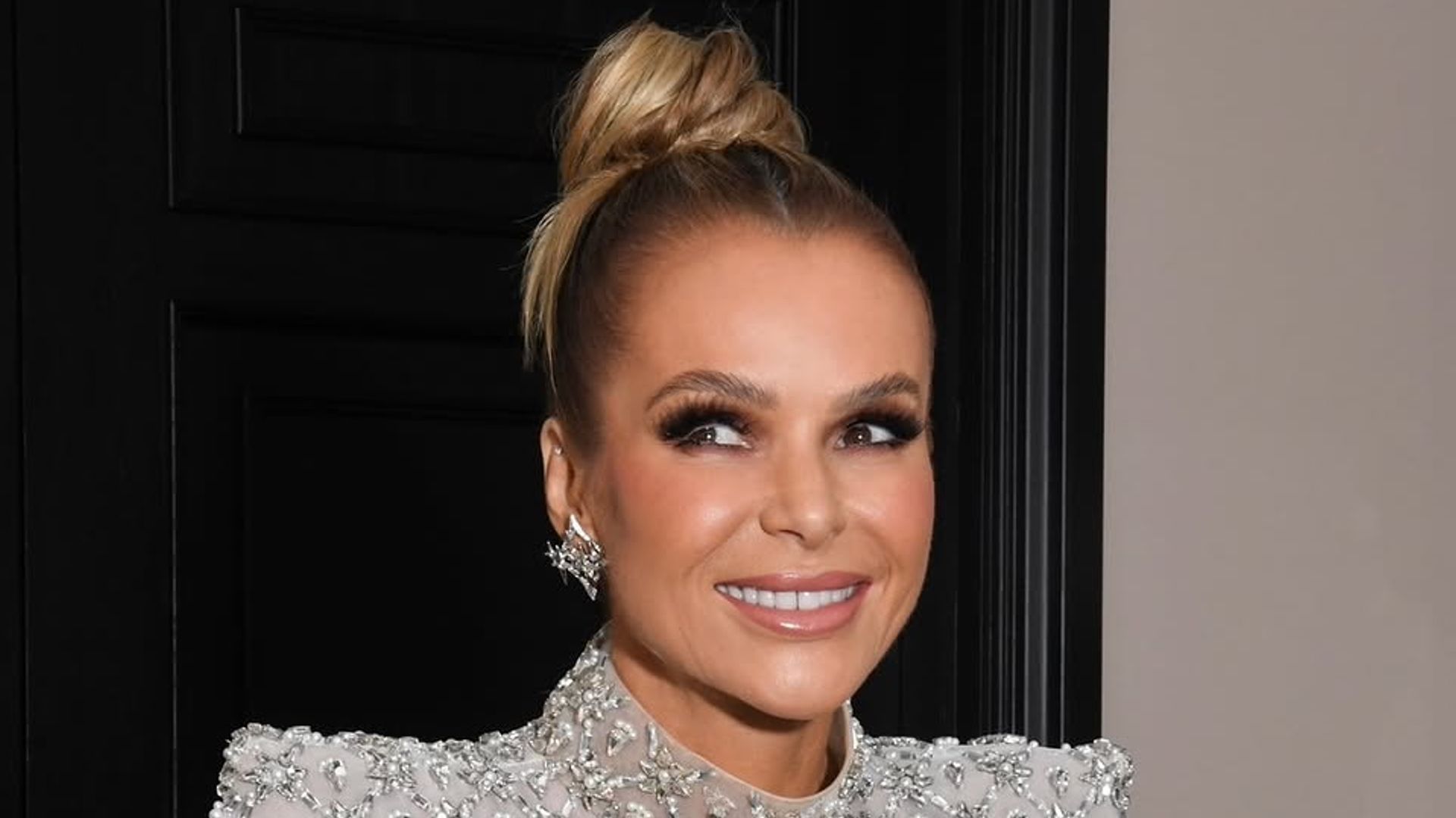 Amanda Holden resting on the banister in her hallway wearing a silver glittery dress and smiling for the camera