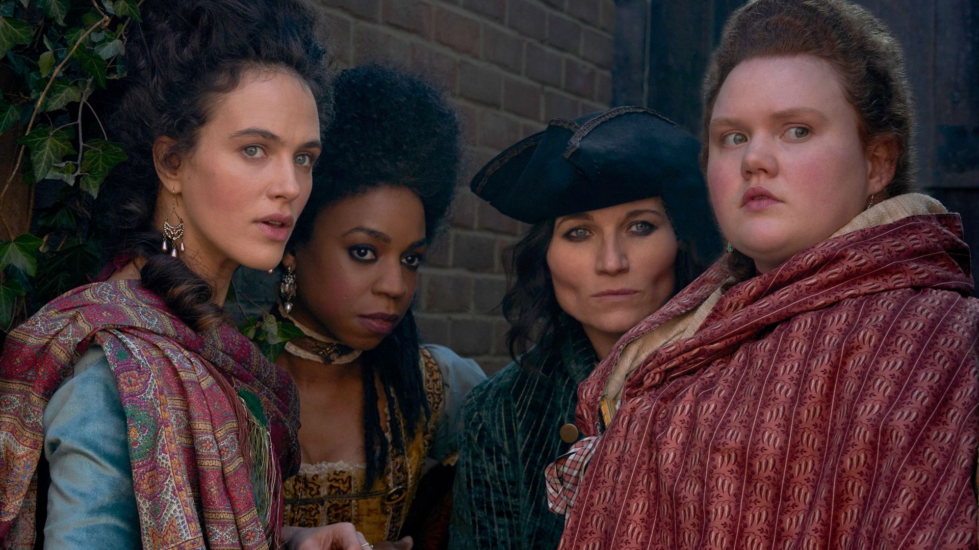 four women in Regency clothing standing by wall