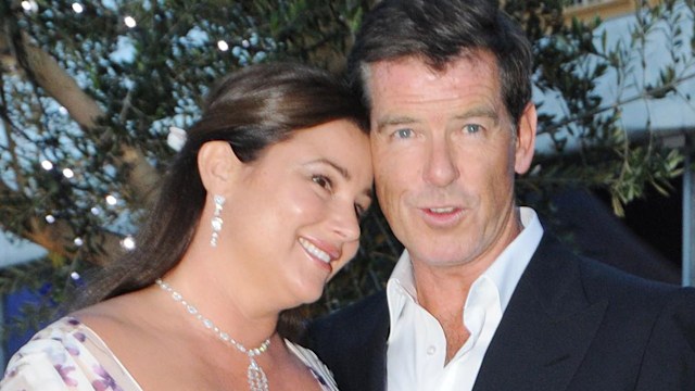 Keely Shaye Smith leaning on Pierce Brosnan's shoulder in a white dress