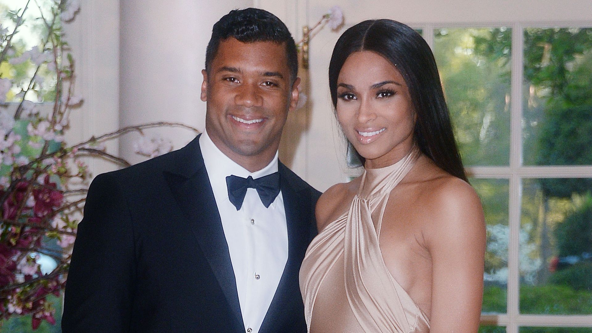 Ciara and Russell smile while wearing black tie attire