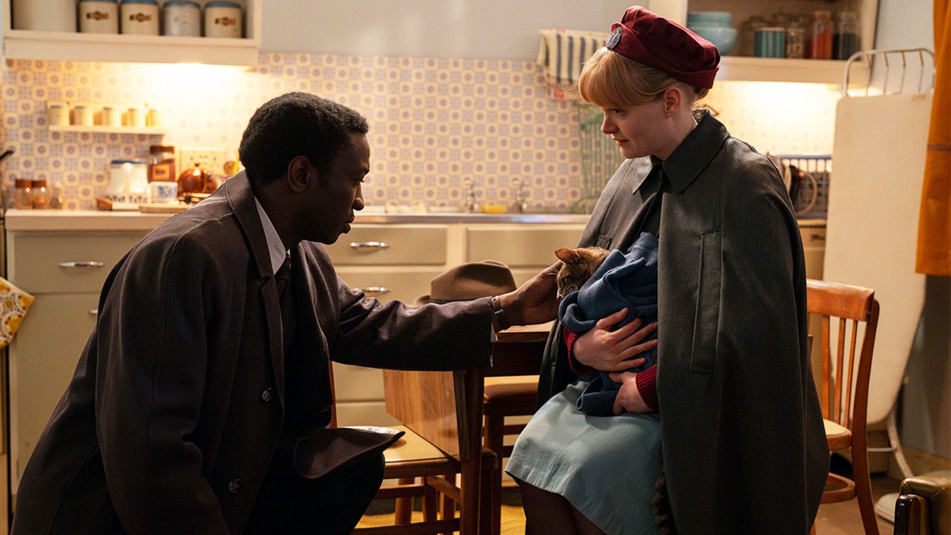 A woman holding a cat while sitting on a chair, a man leaning down to pet the cat