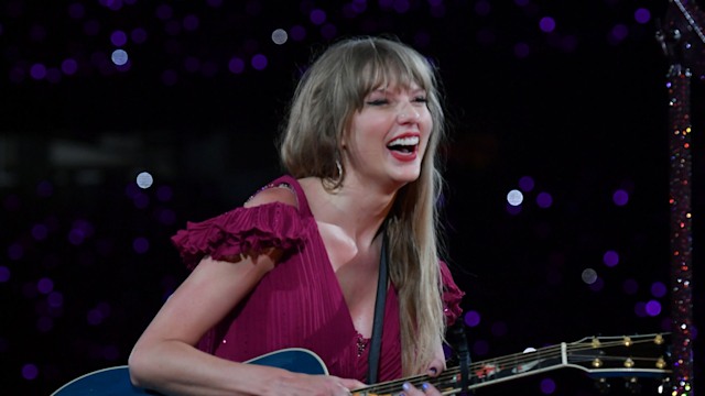 Taylor Swift bending down with her acoustic guitar