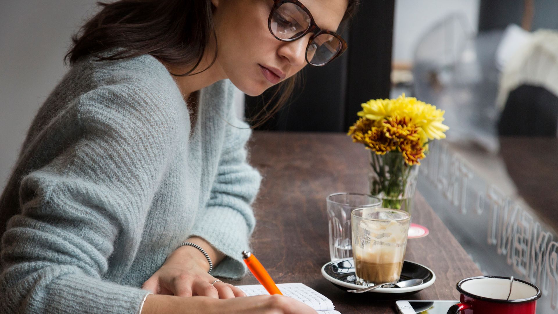 Woman is writing notes, sitting in cafe.