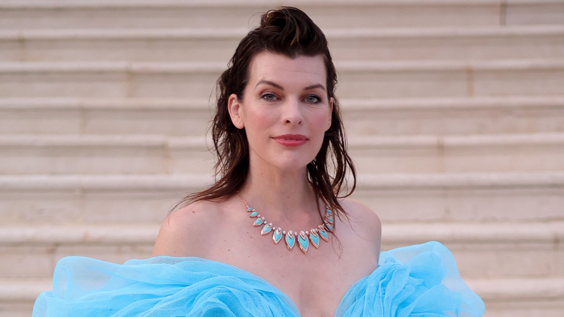 Milla Jovovich smiling in a blue dress on some stairs