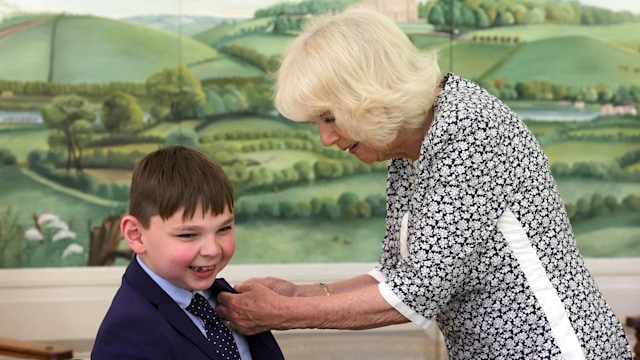 Queen Camilla adjusting the tie of a young boy in a wheelchair