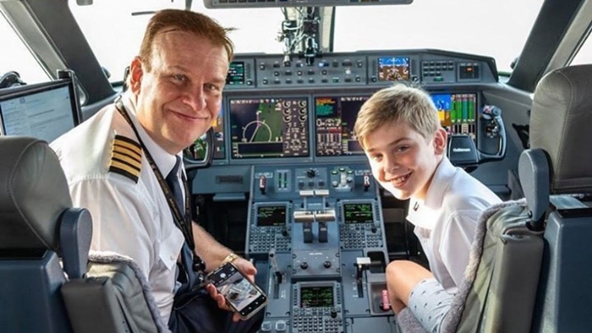 Giles with his dad sat in the pilot's chairs in a plane cockpit