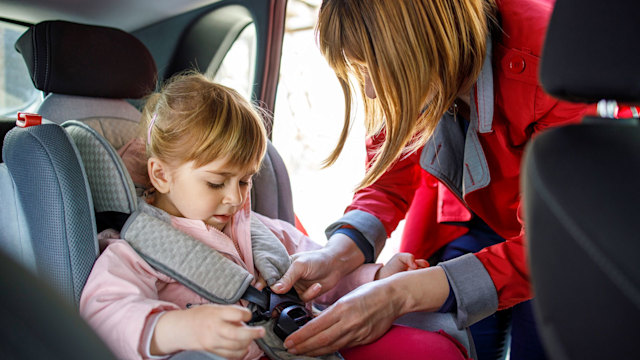 Mum fastening up her daughter in a car seat