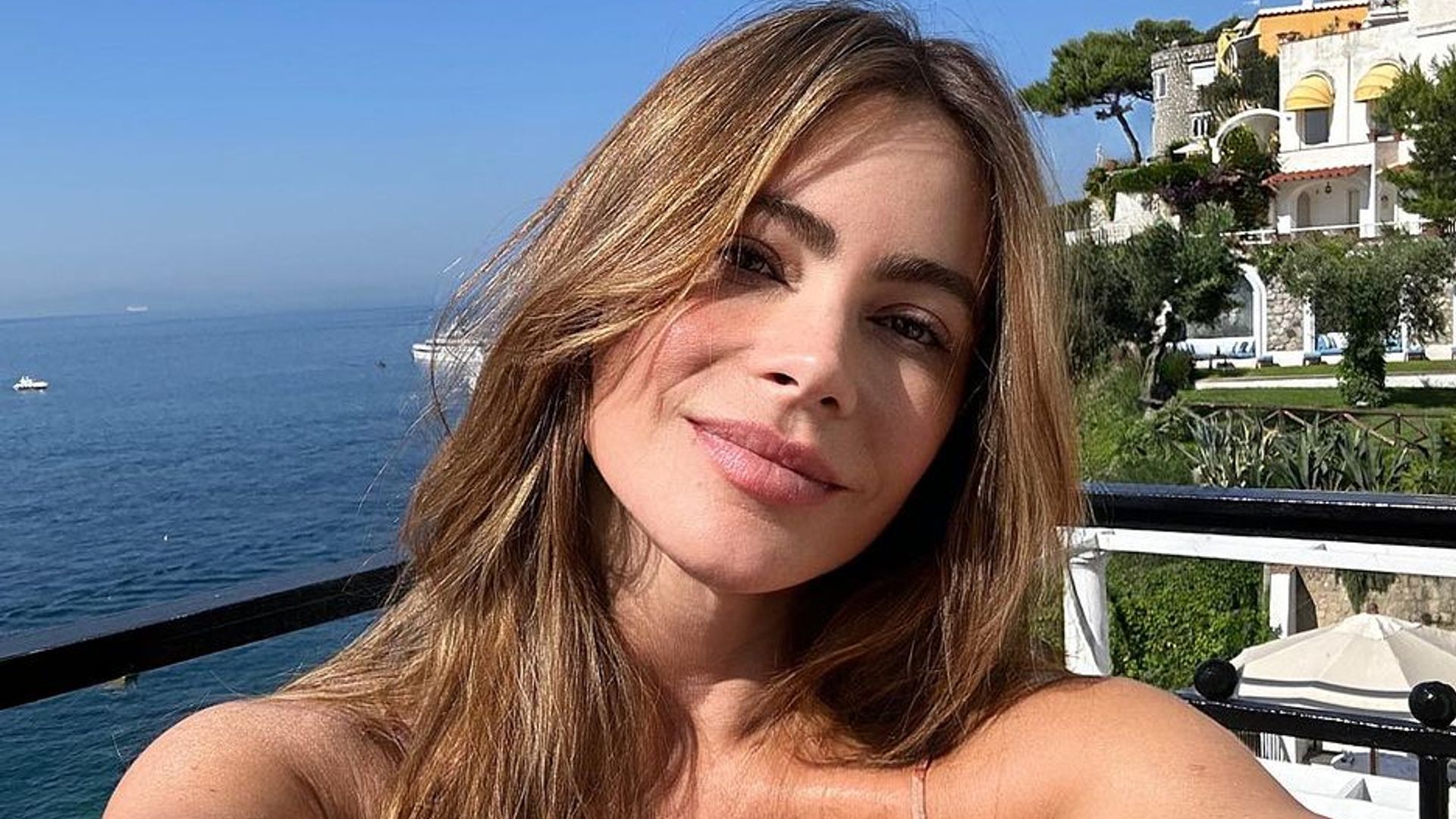 Sofia Vergara in a striped dress taking a selfie from her balcony overlooking the sea