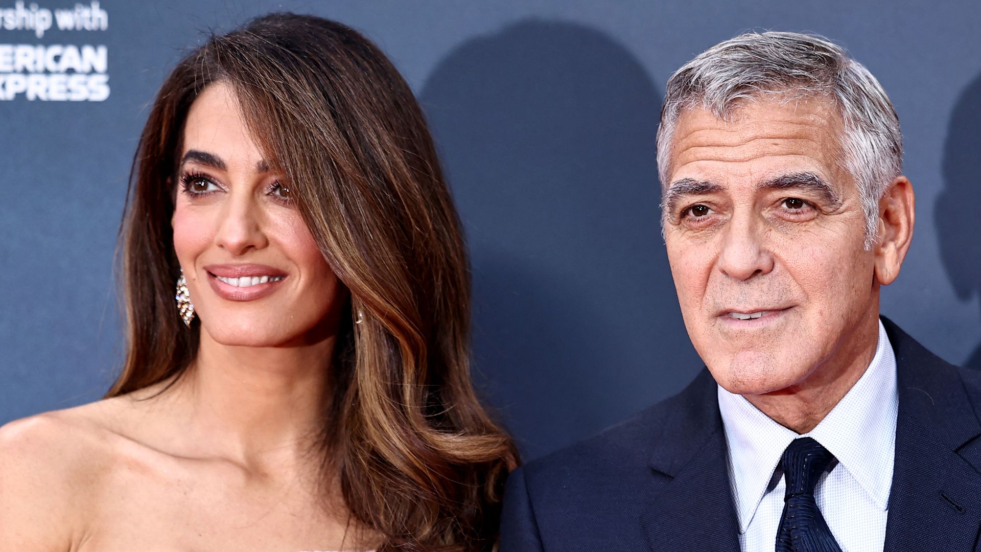 George Clooney poses with his wife Amal Clooney in pink dress