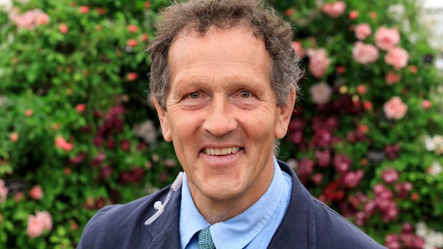 Monty Don smiling in a suit in front of a floral wall