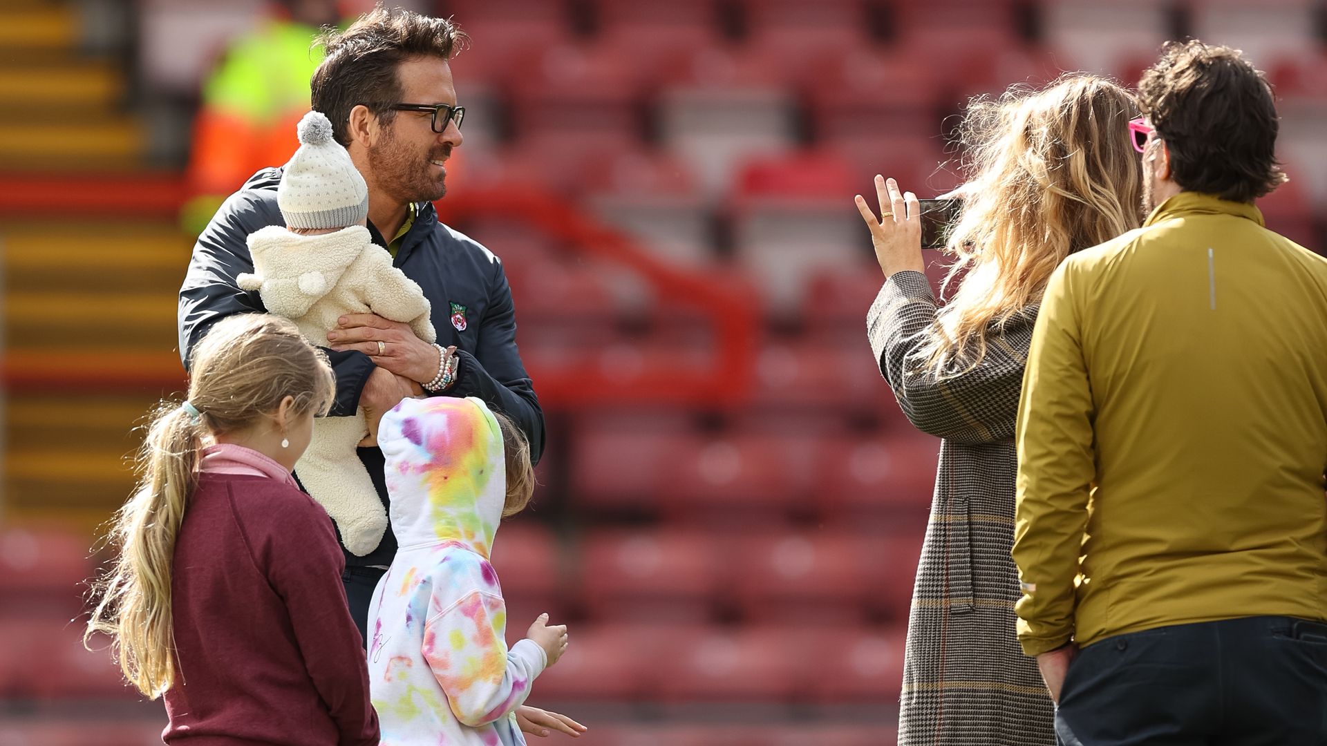 Ryan Reynolds stood holding his newborn, his daughters next to him, Blake Lively is taking a photo of them