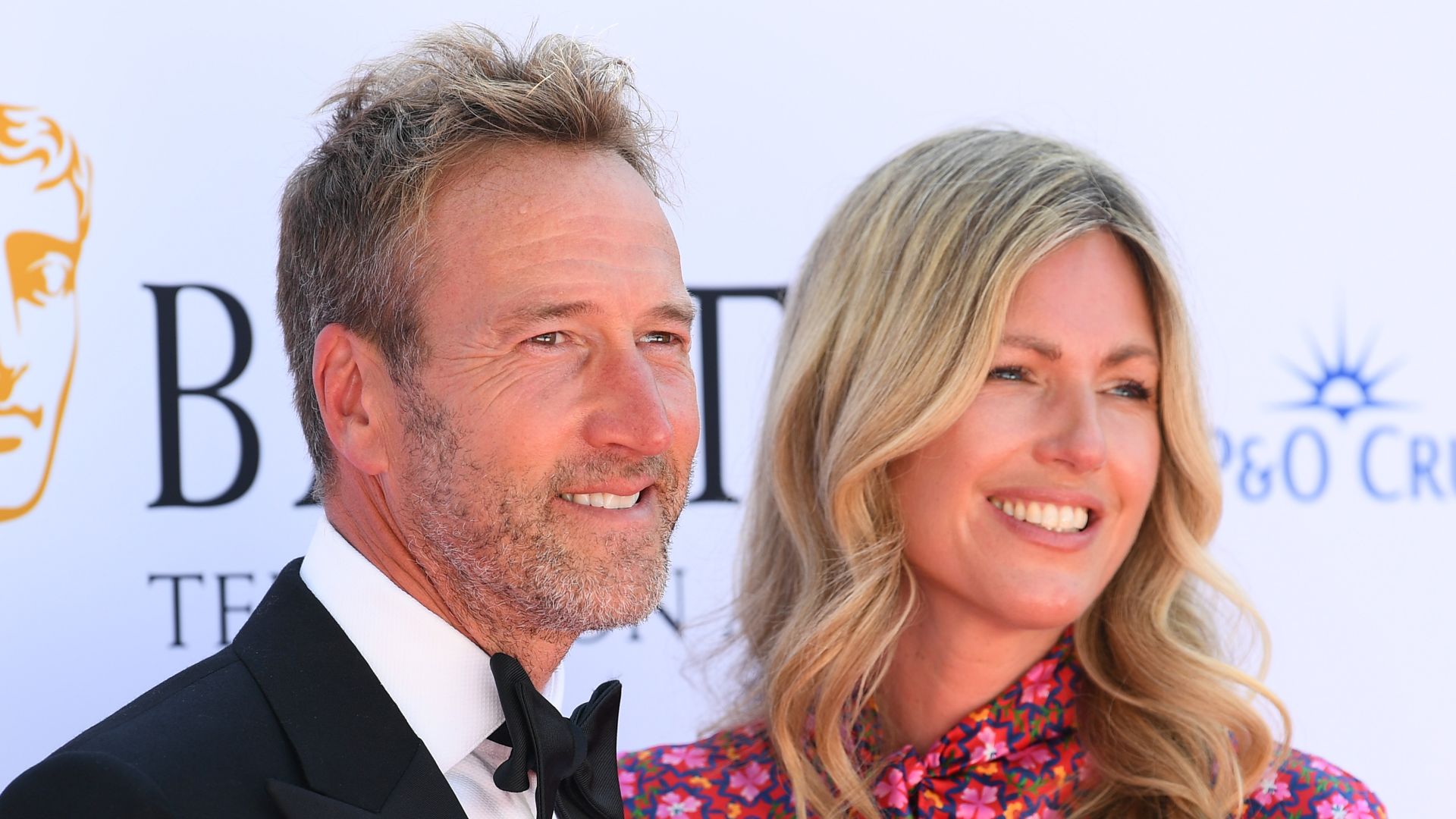 Ben Fogle in black tie and Marina Fogle in floral dress smiling to right 