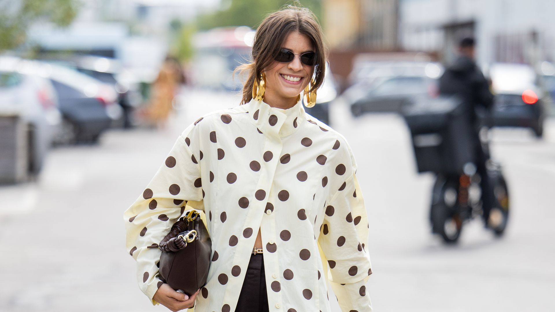 A guest wears dots print beige blouse, brown bag, pants outside Marimekko during Copenhagen Fashion Week 