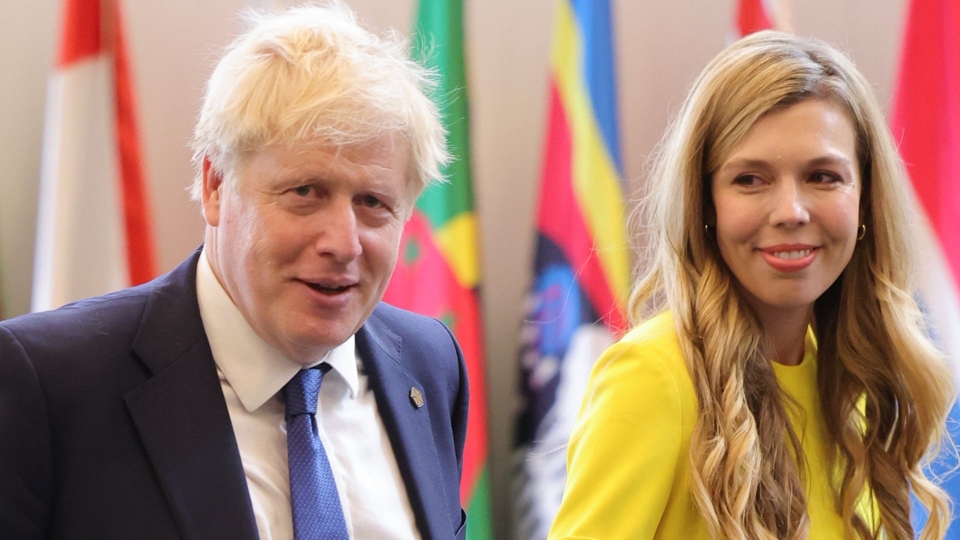 Boris Johnson in a suit walking with Carrie Johnson in a yellow dress