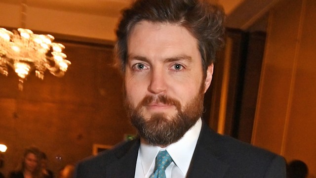 A close-up photo of Tom Burke wearing a suit