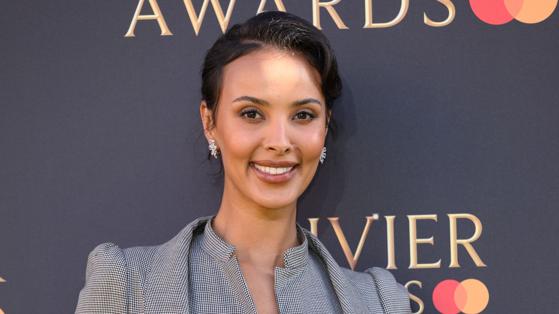 Maya Jama attends The Olivier Awards 2025 at The Royal Albert Hall on April 06, 2025 in London, England wearing a grey suit and updo hairstyle