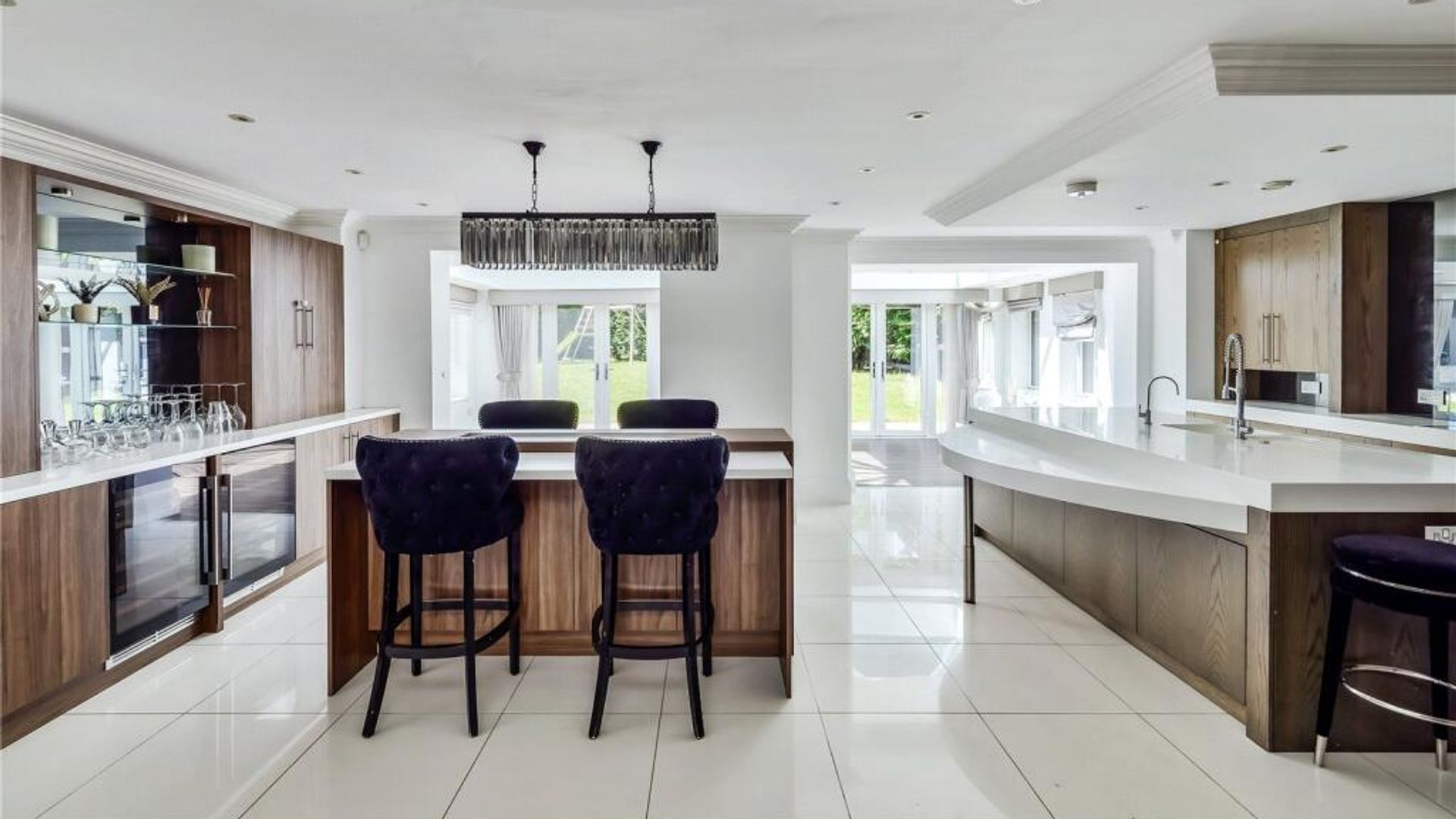 A kitchen with two islands and wood-panelled cupboards and marble-topped surfaces
