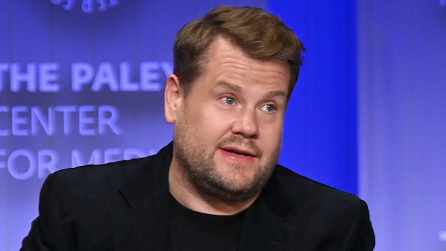 James Corden wearing a black suit sitting on a chair while being interviewed 