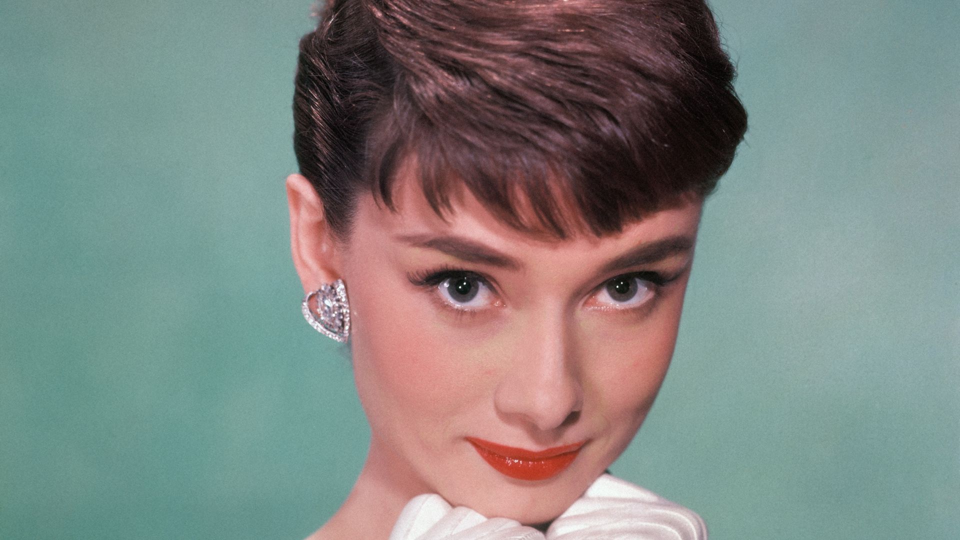Portrait of Belgian-born American actress Audrey Hepburn (1929 - 1993) as she wears a strapless gown and holds white kid-gloved hands up to her chin, early 1950s.