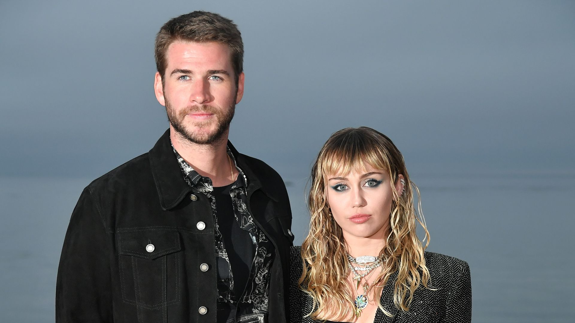 Liam Hemsworth in black denim and Miley Cyrus in gray blazer and ripped pants at the Saint Laurent Mens Spring Summer 20 Show Photo Call