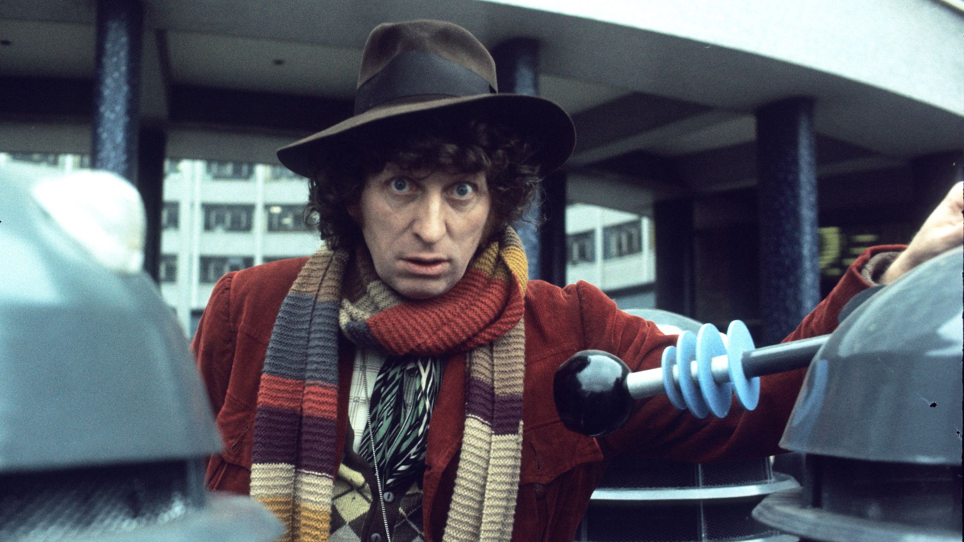 Tom Baker in character as The Doctor with two Daleks