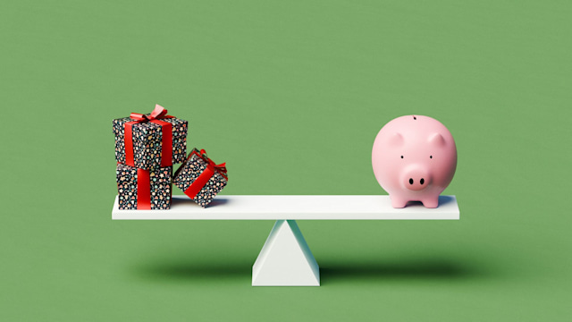 A white seesaw is balanced on a simple background, with a piggy bank on one side and a stack of three Christmas gifts on the other