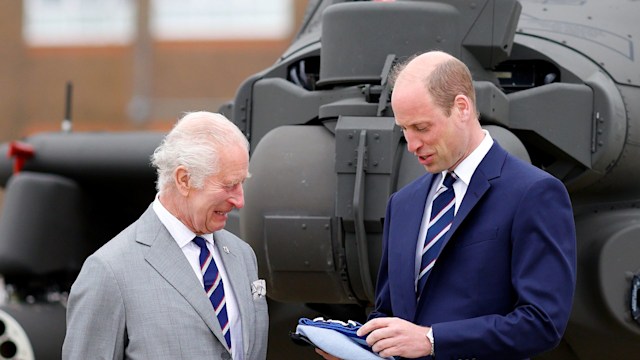 King Charles III and Prince William, Prince of Wales (both wearing the regimental tie of the Army Air Corps) stand in front of an Apache helicopte