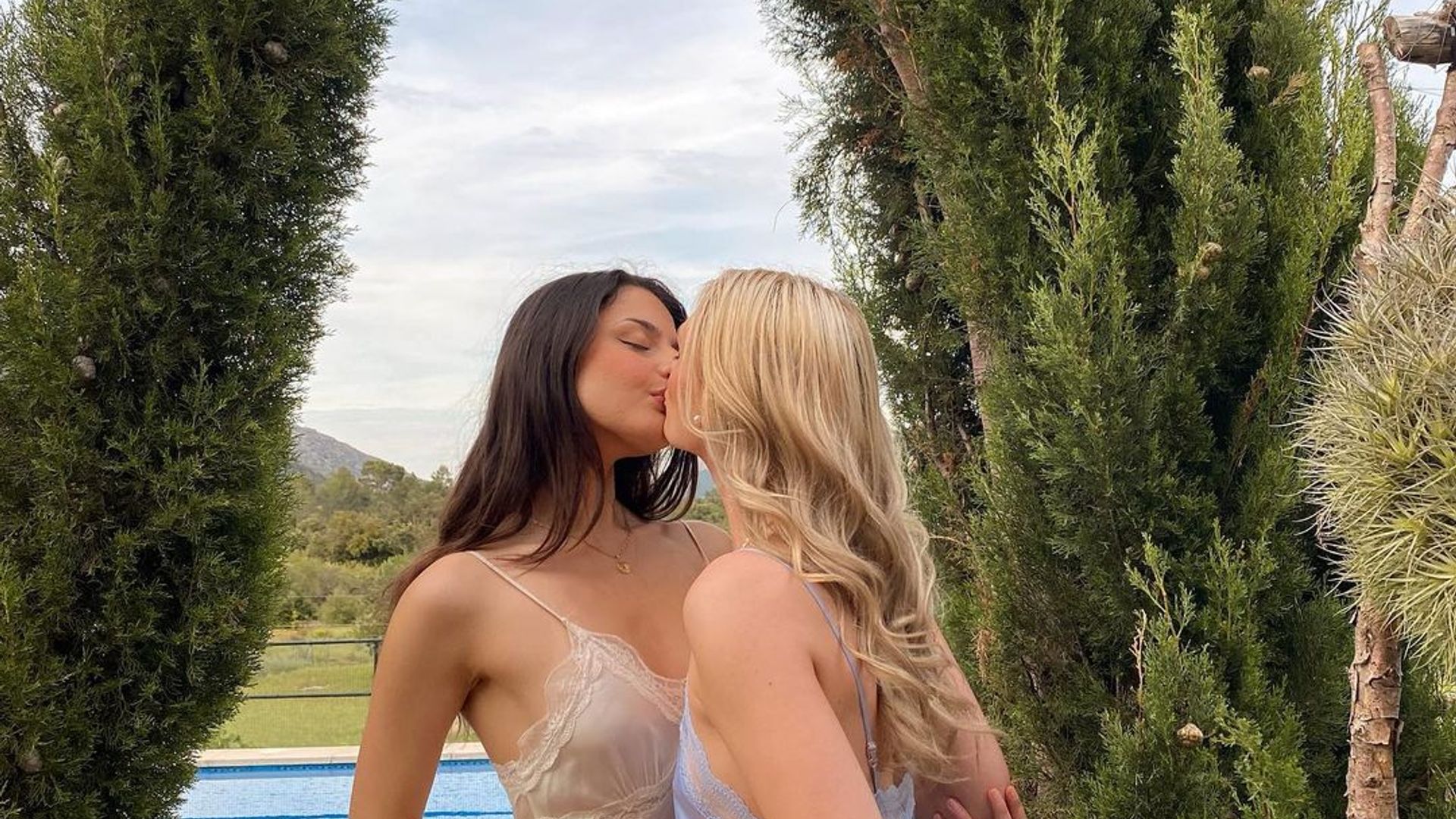 Eden and Emily kissing in front of conifer trees