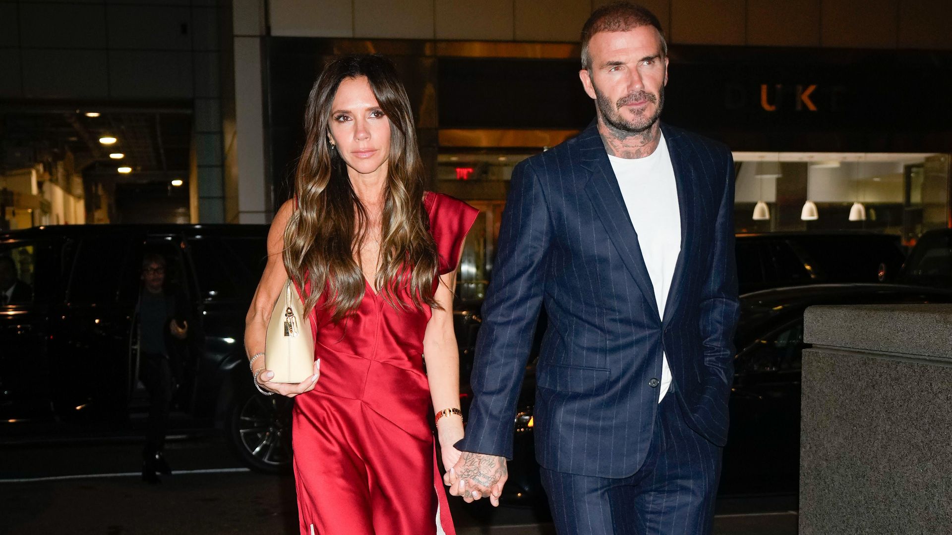 Victoria and David Beckham walking hand in hand in smart clothes